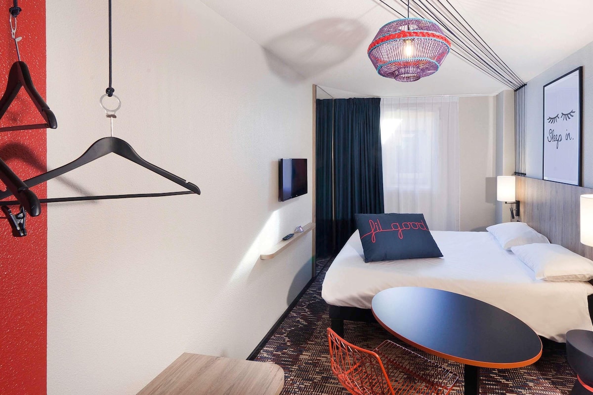 A hotel room with a bed, a TV, a table, and a chair.