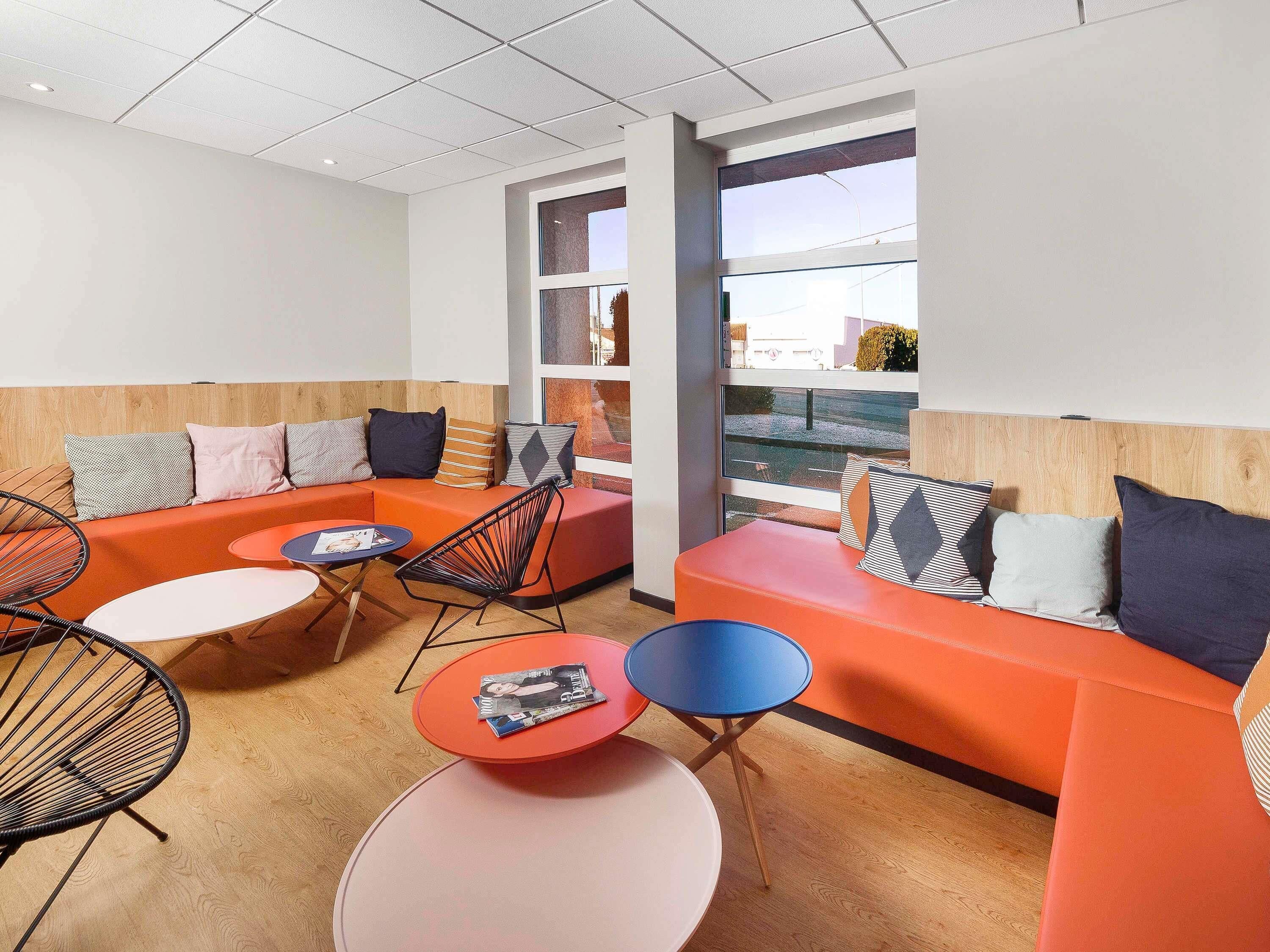 A modern lounge area with a sectional sofa, round tables, and a view through large windows.