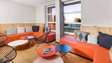 A modern lounge area with a sectional sofa, round tables, and a view through large windows.