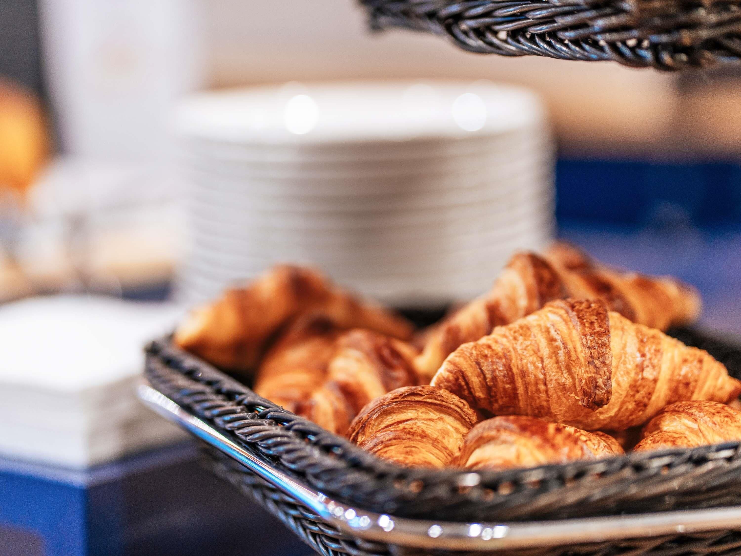 A basket of croissants on a table with stacks of white plates in the background.