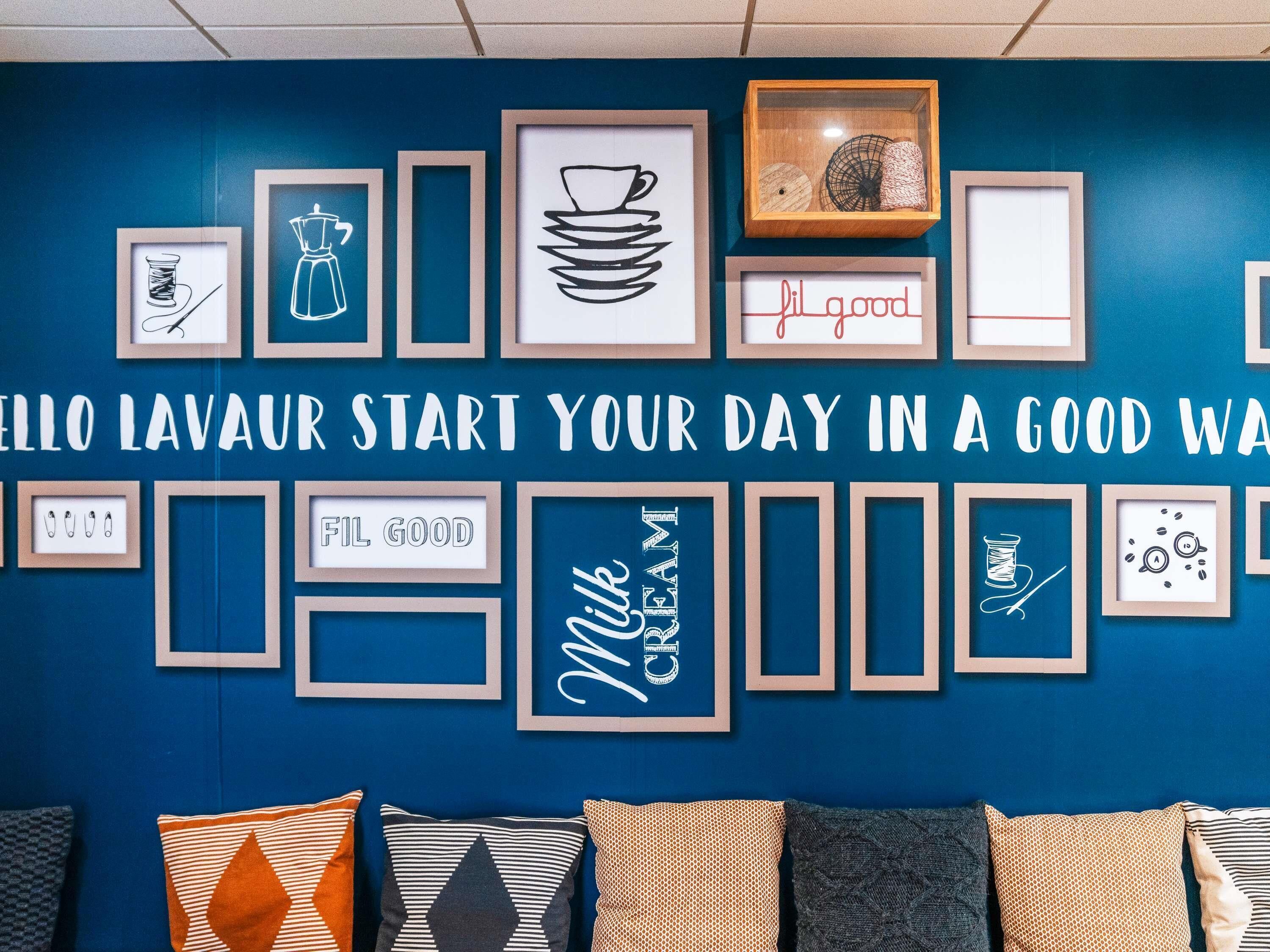 A wall with framed artwork and text, including 'HELLO LAVAU' and 'START YOUR DAY IN A GOOD WAY'.