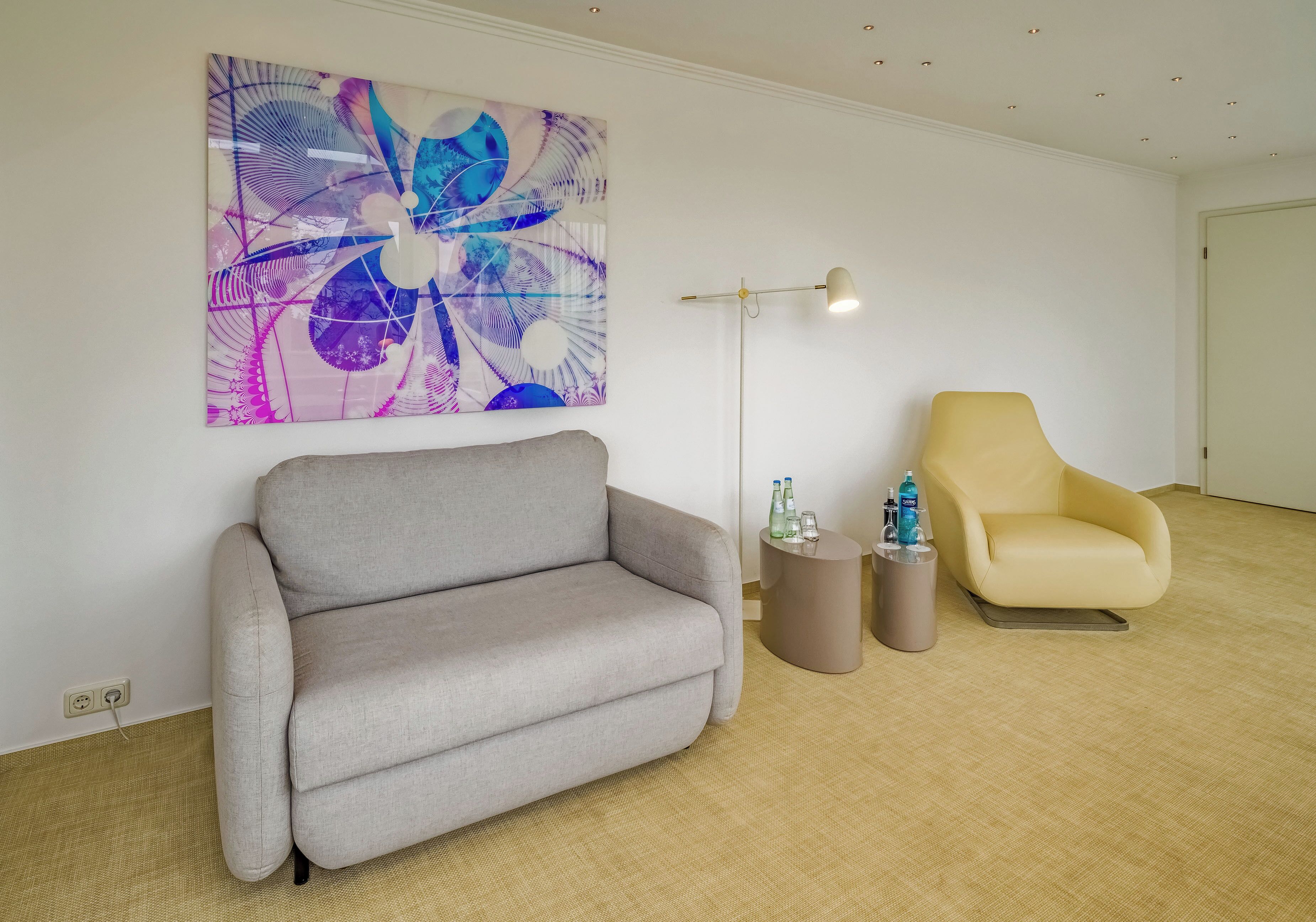 Una sala de estar moderna con un sofá gris, un sillón amarillo, una lámpara de pie y un cuadro abstracto grande en la pared.