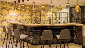 A bar area with a patterned wall, multiple hanging pendant lights, and a counter with stools. - rugs HOTEL Köln (Cologne)