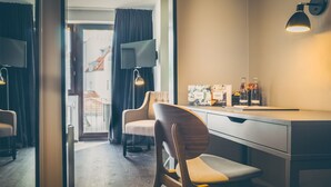 A modern hotel room with a desk, two chairs, a flat-screen TV, and a view of buildings outside. - rugs HOTEL Köln (Cologne)