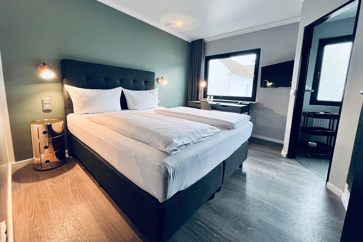 A modern hotel room with a large bed, a desk, and a window.
