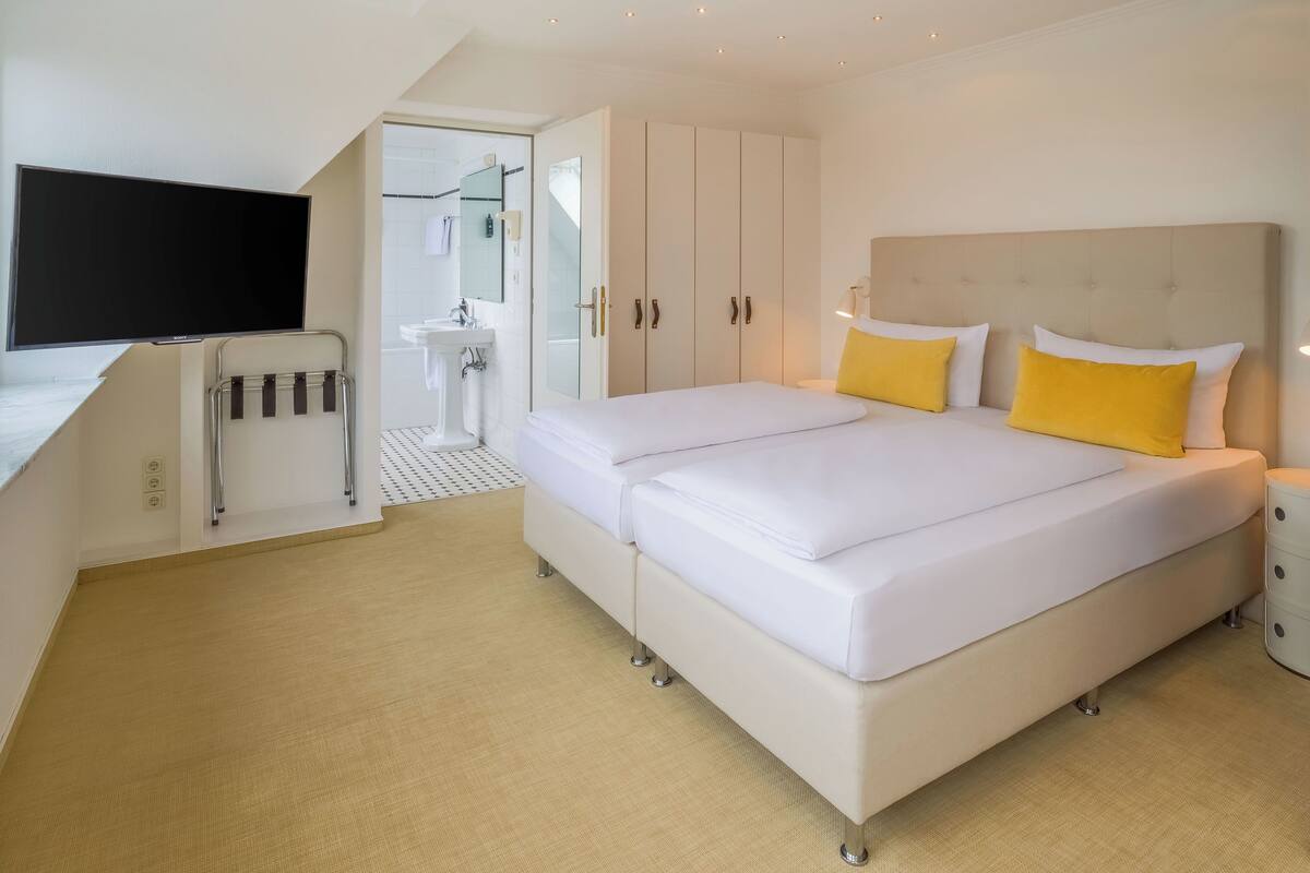 A modern hotel room with a large bed, bedside tables, a TV, a bathroom with a sink and shower, and a walk-in closet.