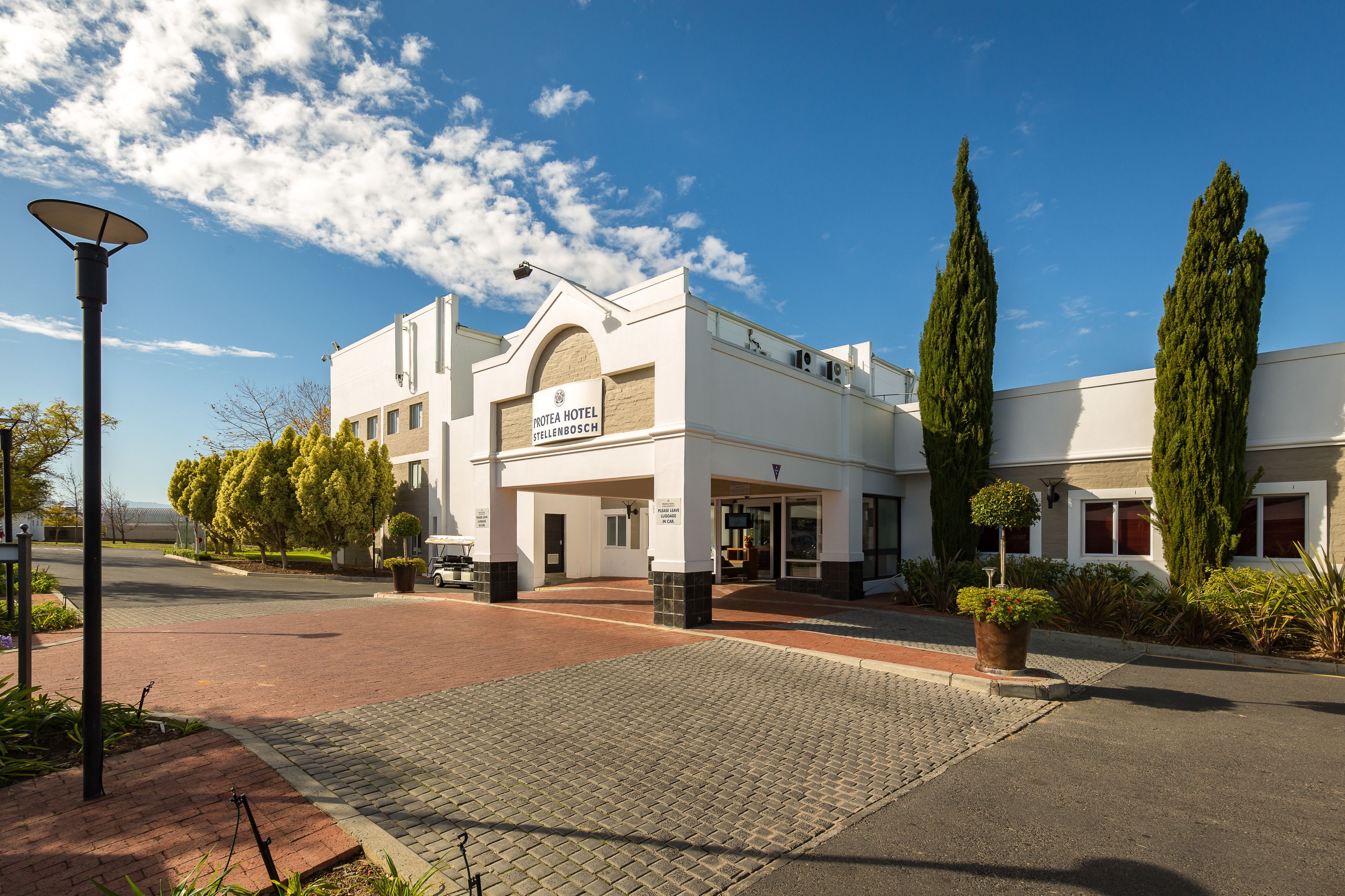 Un hotel con fachada blanca, entrada abovedada y un letrero que dice 'HOTEL STELLENBOSCH'.