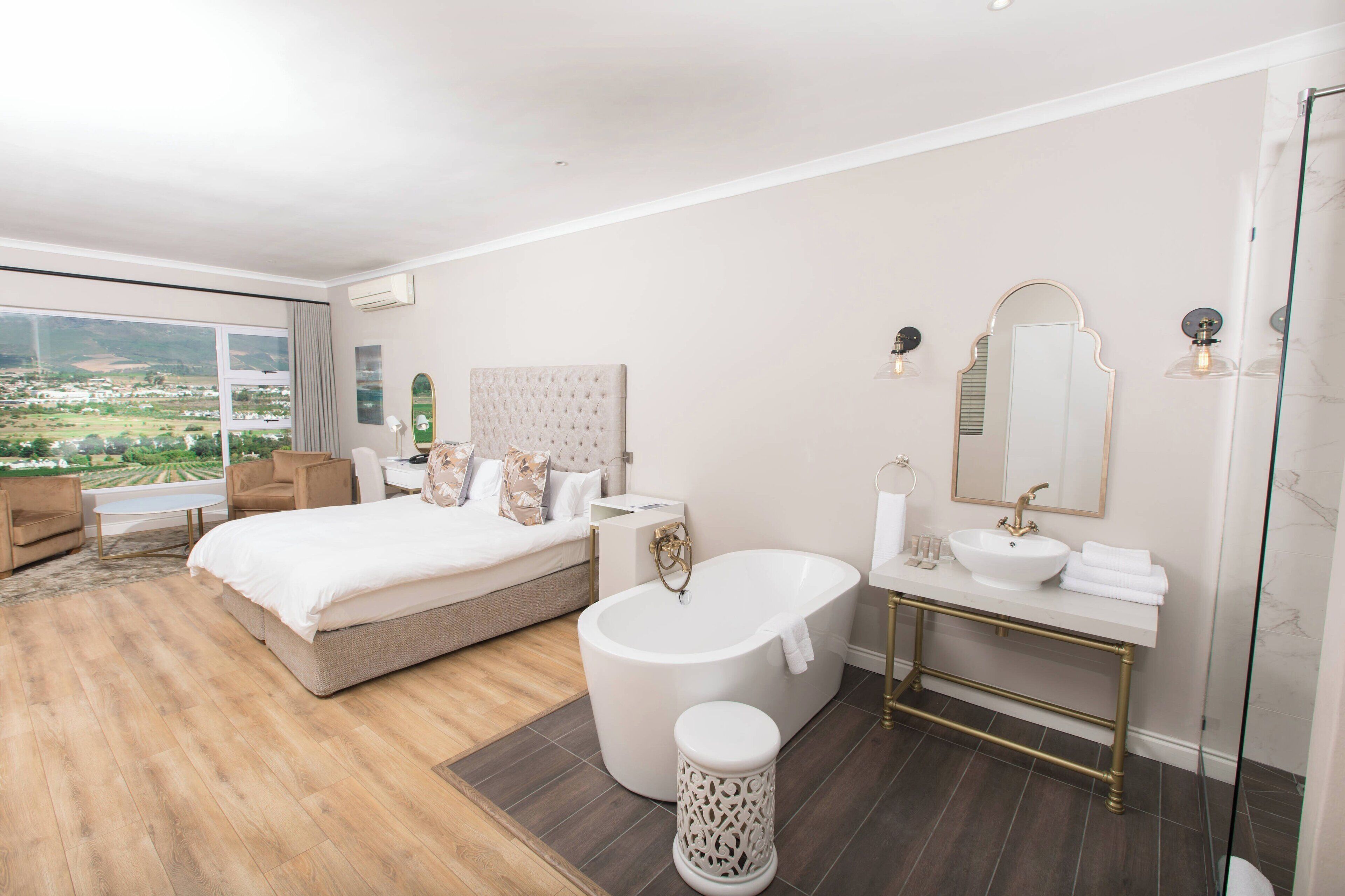 Un dormitorio moderno con una cama grande, una zona de estar, una bañera y un baño con un espejo grande y lavamanos.