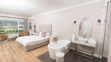 Un dormitorio moderno con una cama grande, una zona de estar, una bañera y un baño con un espejo grande y lavamanos.