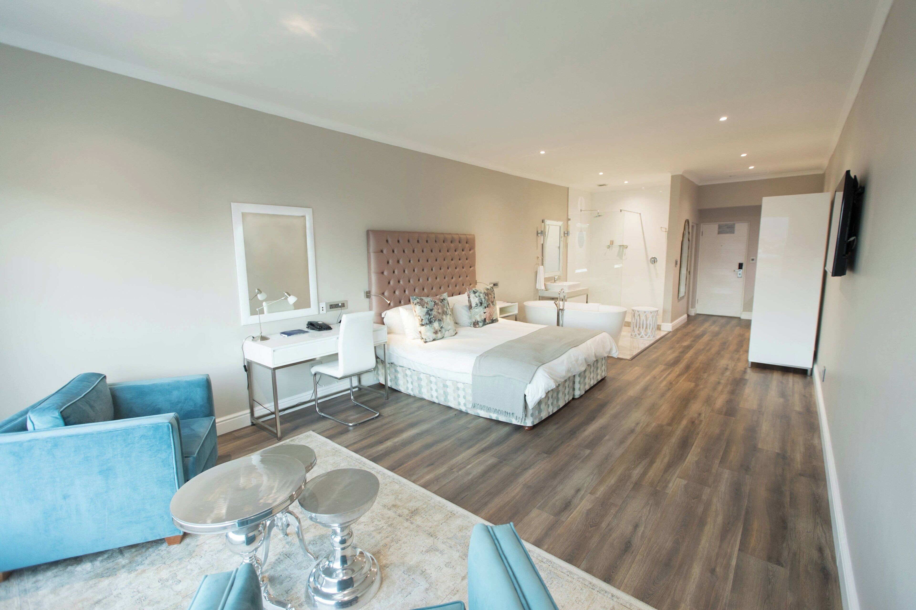 A modern hotel room with a large bed, a desk, a chair, and a dining table.