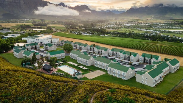 Een groot hotelcomplex met meerdere gebouwen, een zwembad en uitzicht op omliggende bergen en velden.