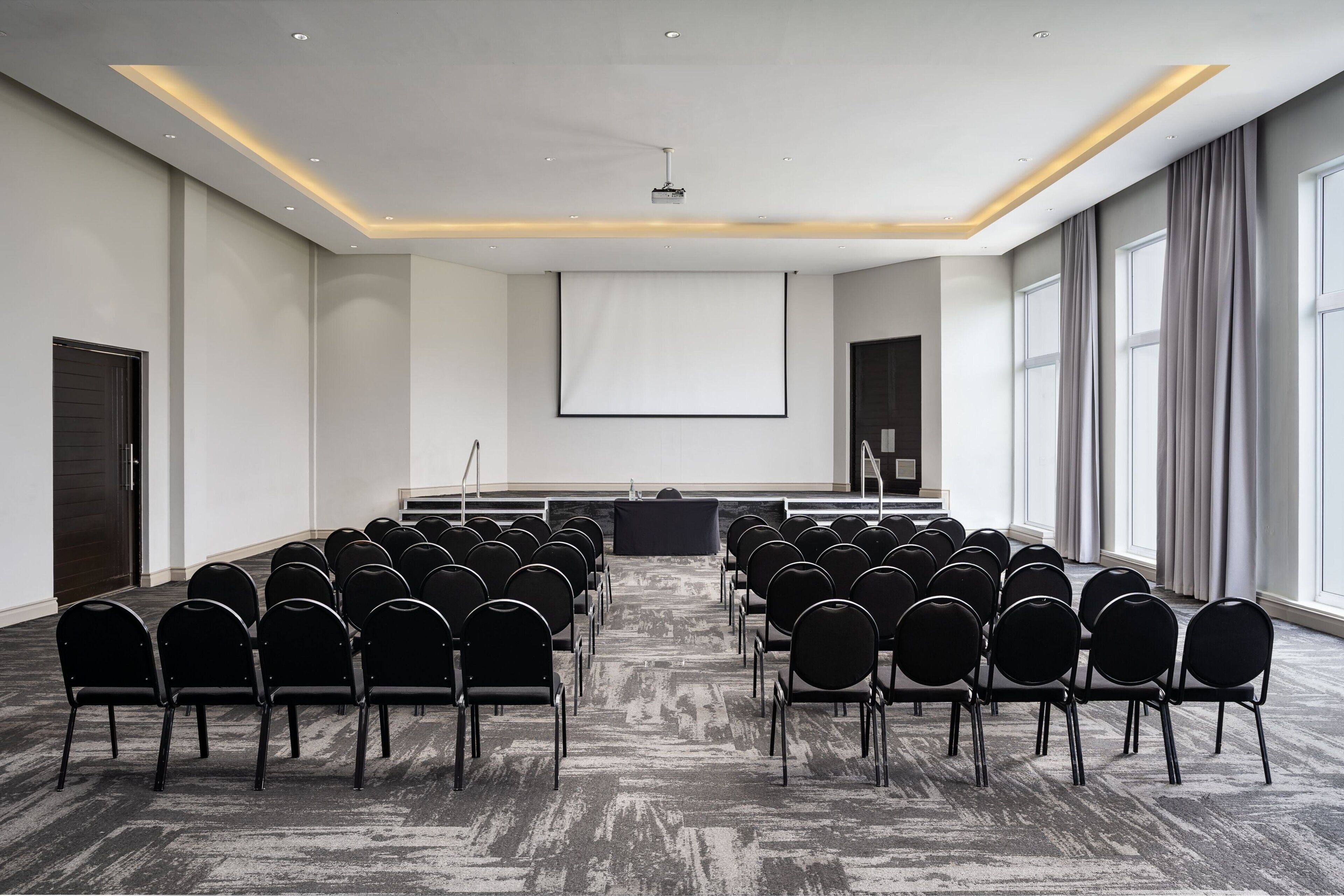 A conference room with rows of chairs facing a large screen, a podium, and a projector.