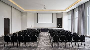 A conference room with rows of chairs facing a large screen, a podium, and a projector.