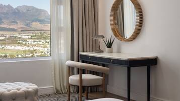 Un dormitorio con vistas a un paisaje montañoso, un escritorio con una lámpara, una silla y un reposapiés tapizado.