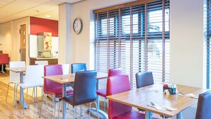 Un espace repas avec des tables et des chaises, une horloge au mur et une fenêtre avec des stores.