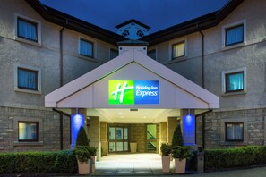 A Holiday Inn Express hotel entrance with a modern design, featuring a prominent sign, a covered walkway, and potted plants.