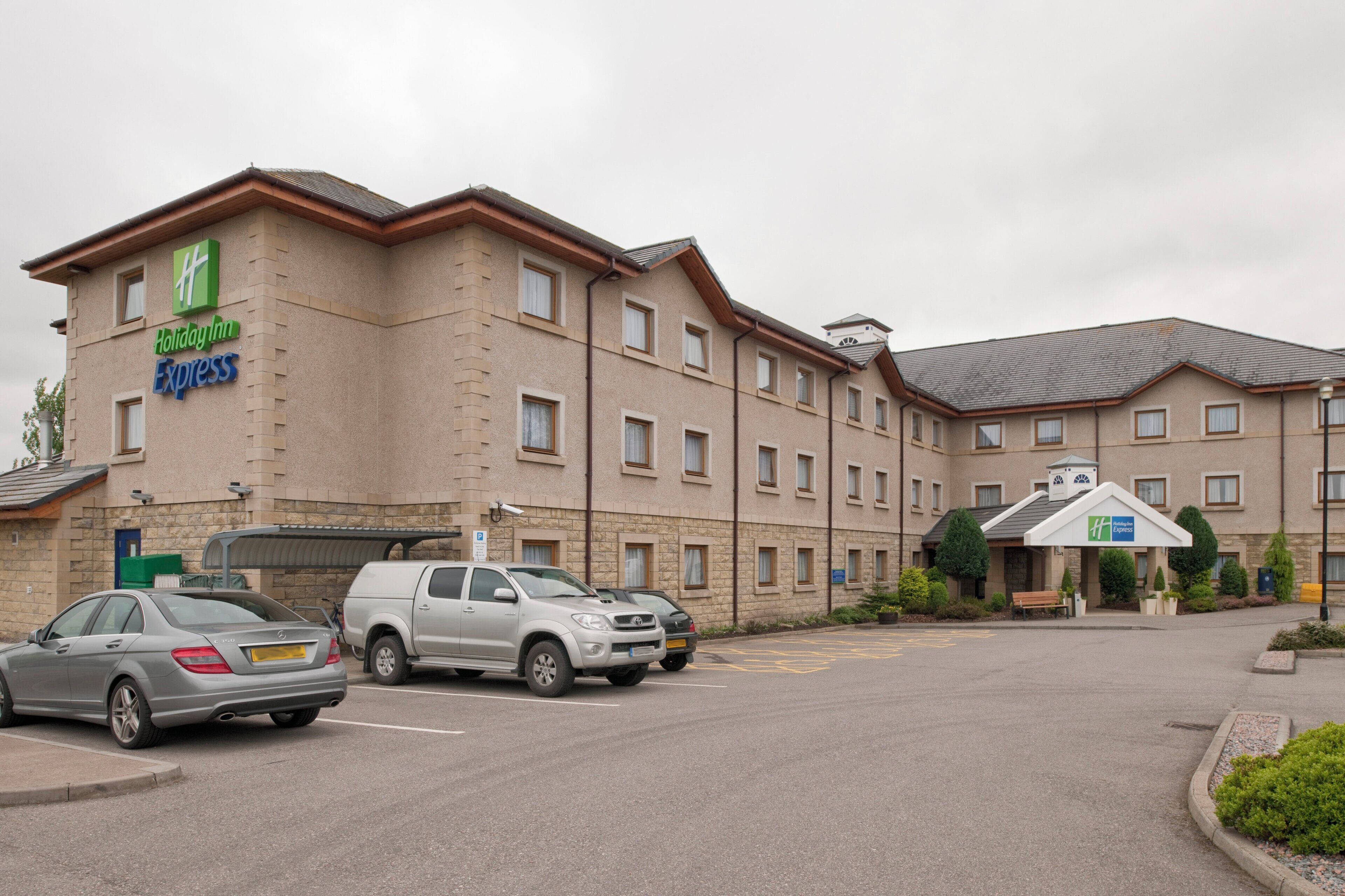 A Holiday Inn Express hotel with a parking lot, multiple cars, and a building with a stone facade.