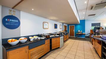 A breakfast area with a buffet setup, including bowls of fruit and a variety of food items.