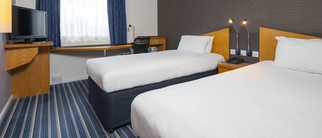 A hotel room with two beds, a desk with a TV, a chair, and a window with curtains.