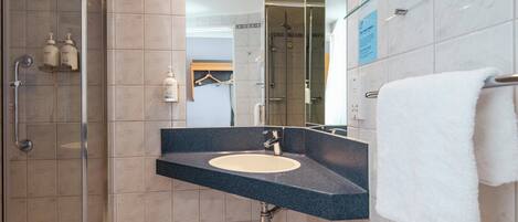 Un baño moderno con cabina de ducha de vidrio, lavabo con encimera oscura y perchero para toallas.