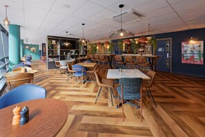 A modern restaurant with wooden flooring, blue and brown chairs, and a bar area. - Travelodge Slough (Slough)