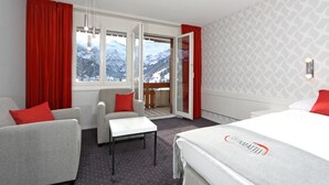 A hotel room with a bed, two armchairs, a small table, and a balcony with a mountain view. - Hotel Steinmattli (Adelboden)