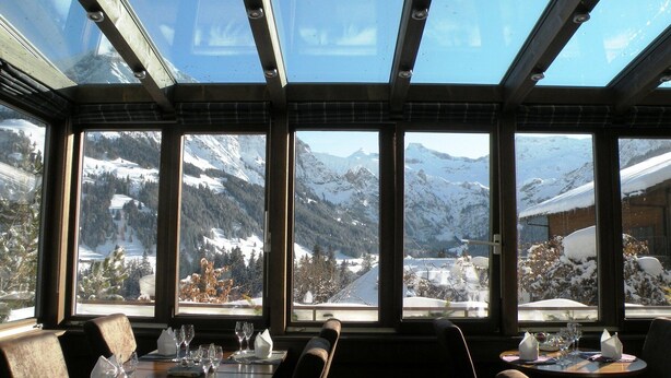A restaurant with a mountain view, large windows, and a table set for dining. - Hotel Steinmattli (Adelboden)