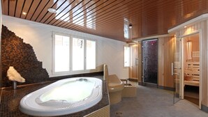 A modern spa room with a hot tub, wooden ceiling, and a glass door leading to a sauna area. - Hotel Steinmattli (Adelboden)