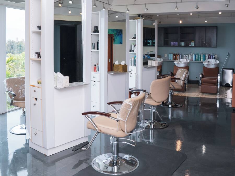 A modern salon with multiple hairdressing stations, a large window, and a view of greenery outside.