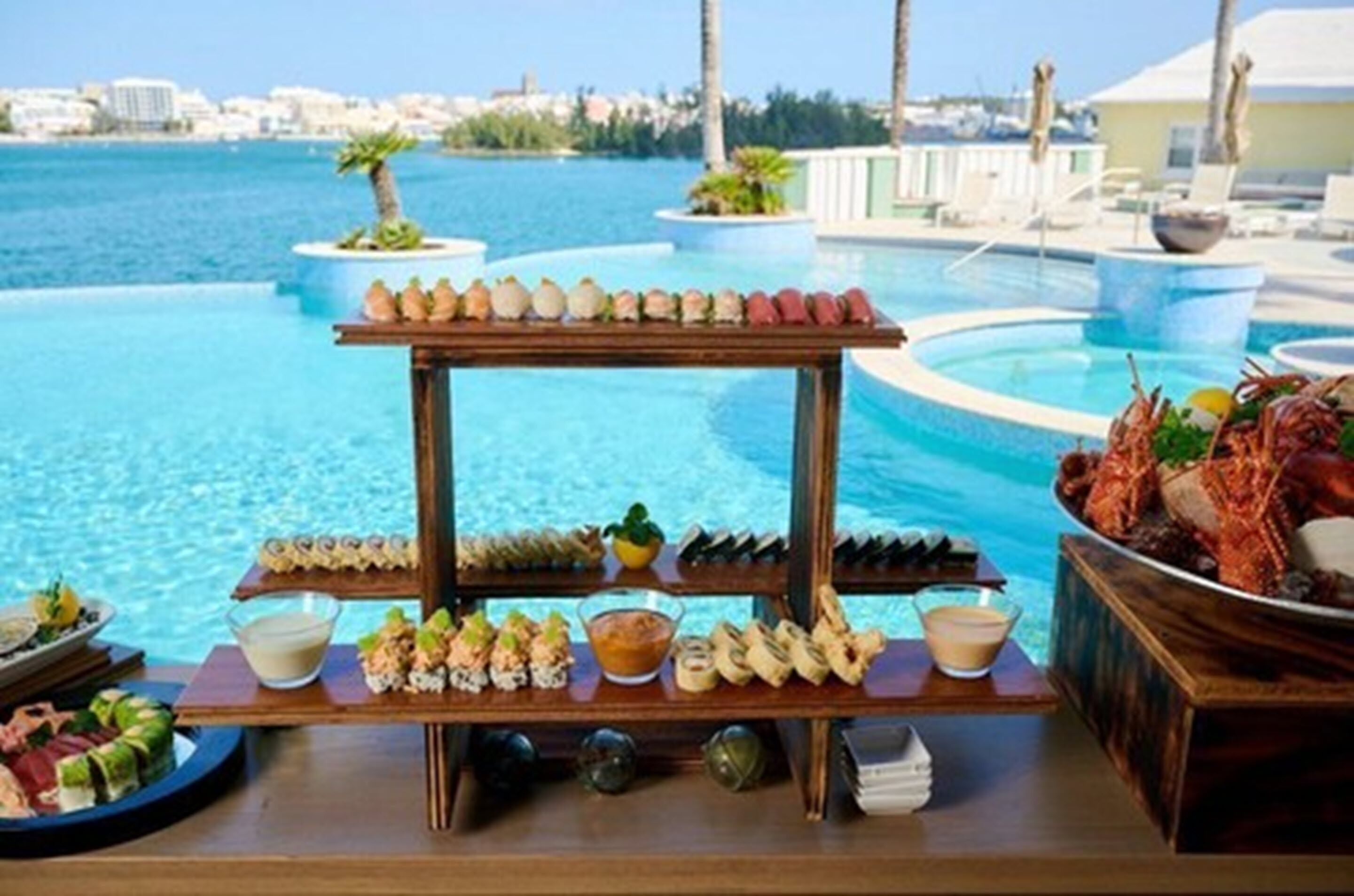 A buffet table with seafood and appetizers by a pool with a city view.