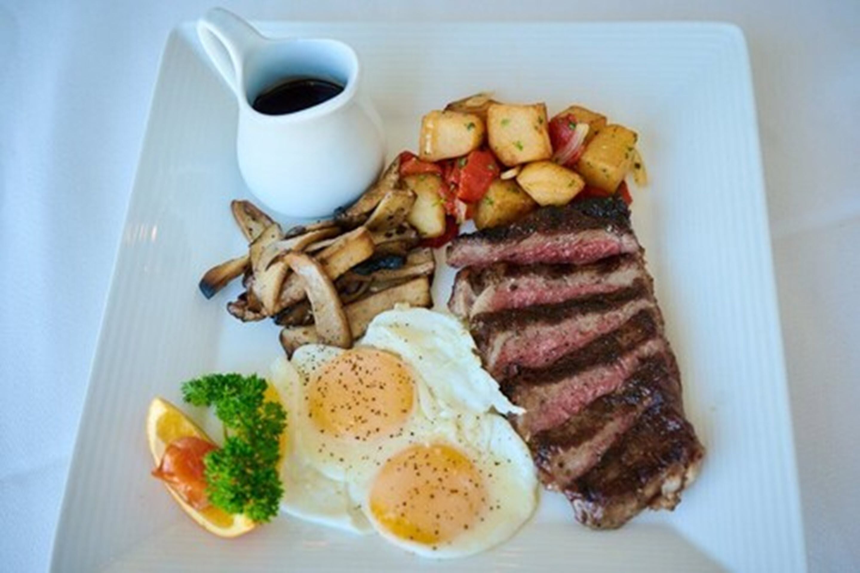 Un plato con bistec, huevos, champiñones y papas.