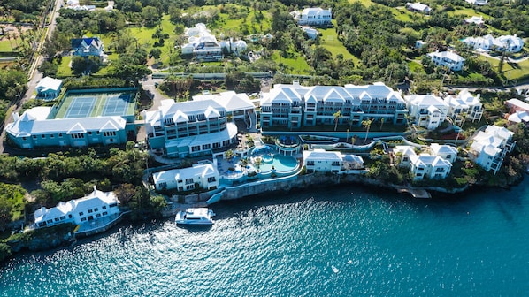 An aerial view of a coastal resort with multiple buildings, a swimming pool, and a dock with a boat. - Newstead Belmont Hills Golf Resort & Spa (Paget Parish)