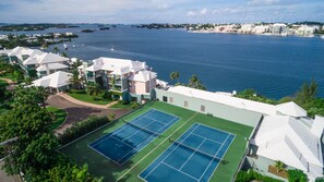A resort with tennis courts, a pool, and a view of the ocean.