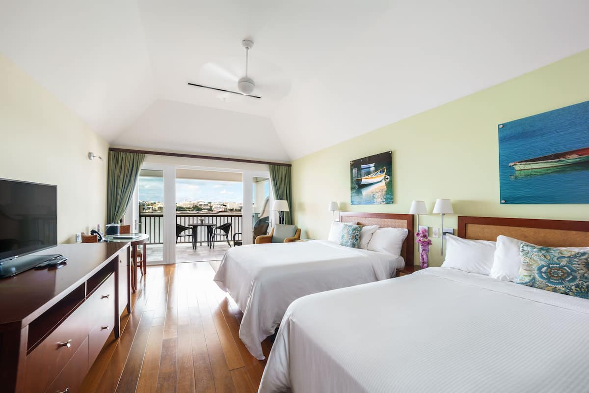 A hotel room with two beds, a TV, a desk, and a balcony with a view.