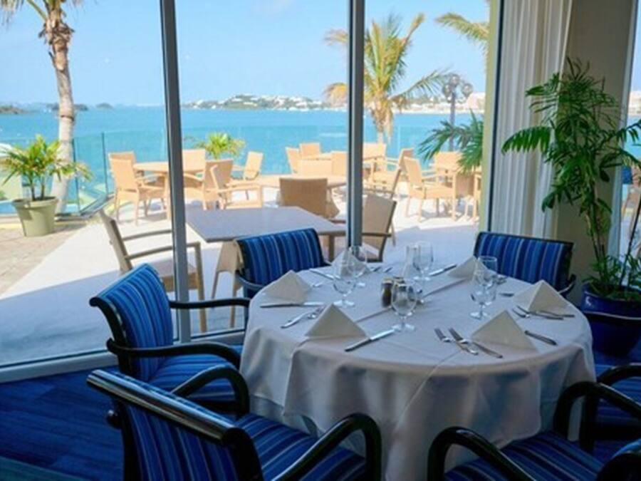 A dining area with a table set for four, overlooking a beach with palm trees and the sea.