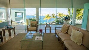 Una sala moderna con una mesa de centro de vidrio, un sofá color beige y vistas al océano.