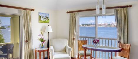 A room with a view of the sea, a chair, a table, and a lamp.