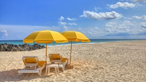 Una playa con dos sombrillas amarillas y dos sillas reclinables blancas.