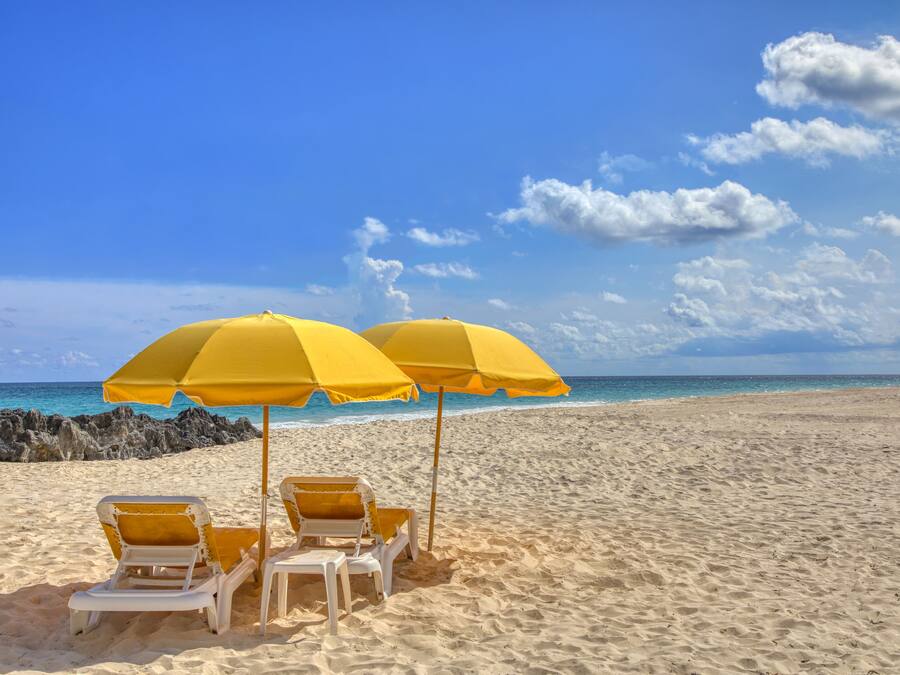 Una playa con dos sombrillas amarillas y dos sillas reclinables blancas.