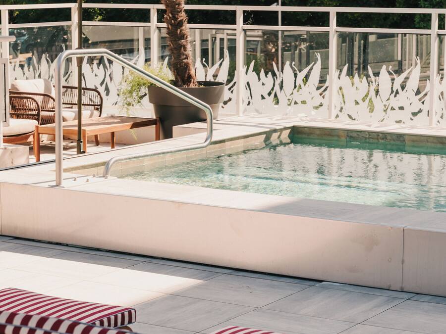 Zona de piscina con sillones de descanso, una palmera y una cerca decorativa blanca.