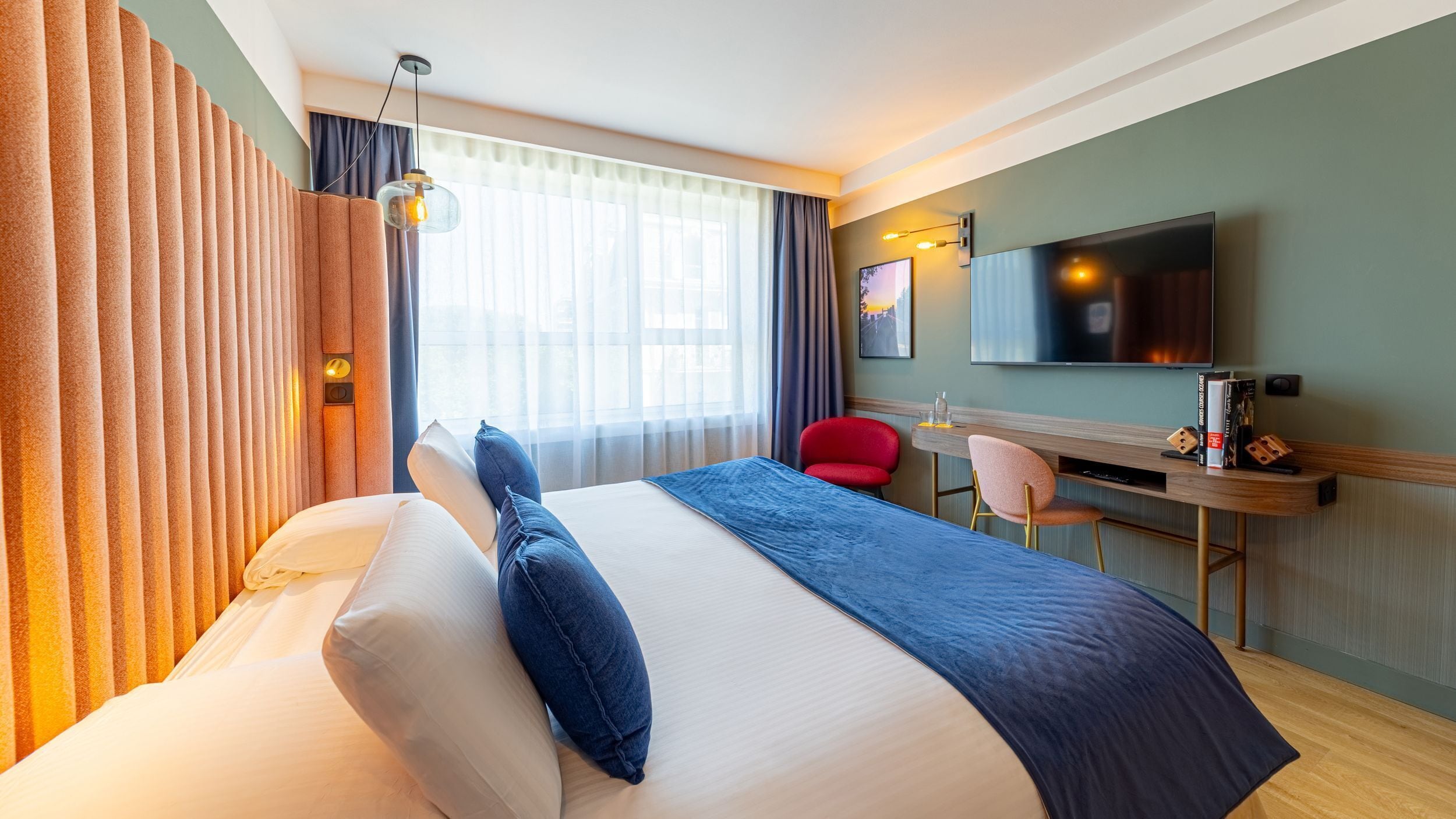 Una habitación de hotel con una cama grande, un escritorio con silla, televisión y ventana con cortinas.
