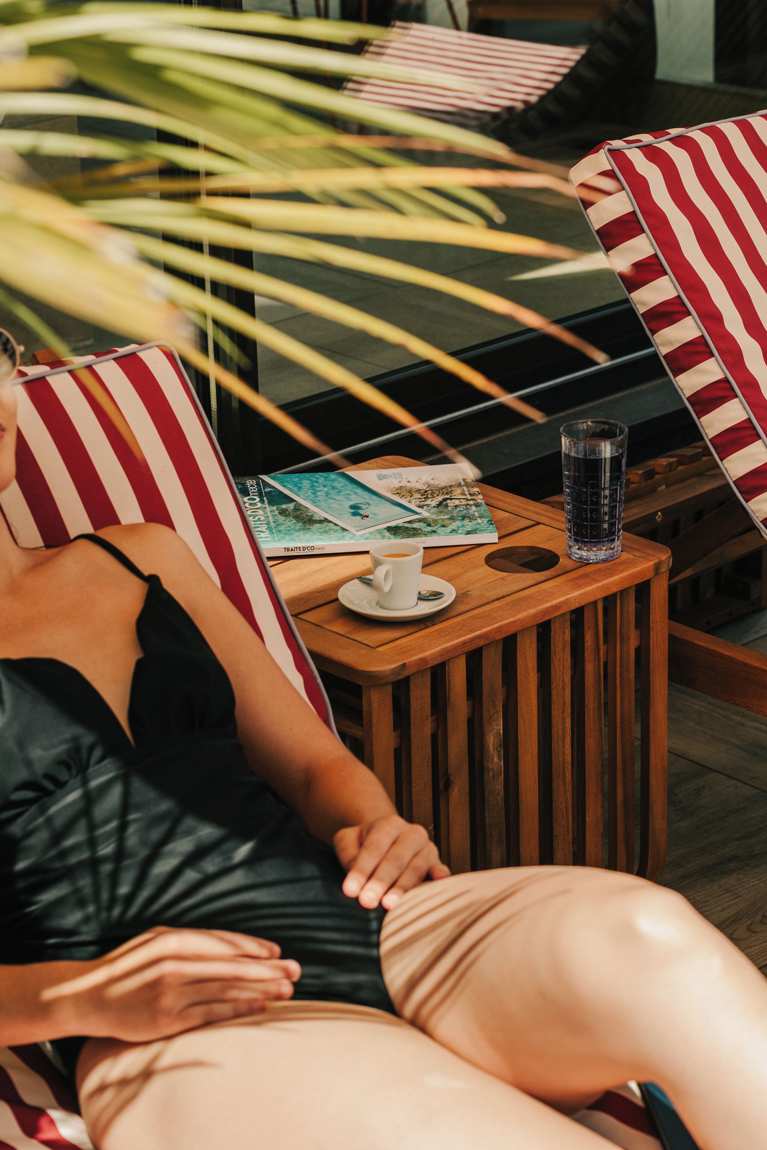 A person reclining on a striped chair with a book, a glass of water, and a cup on a wooden side table.