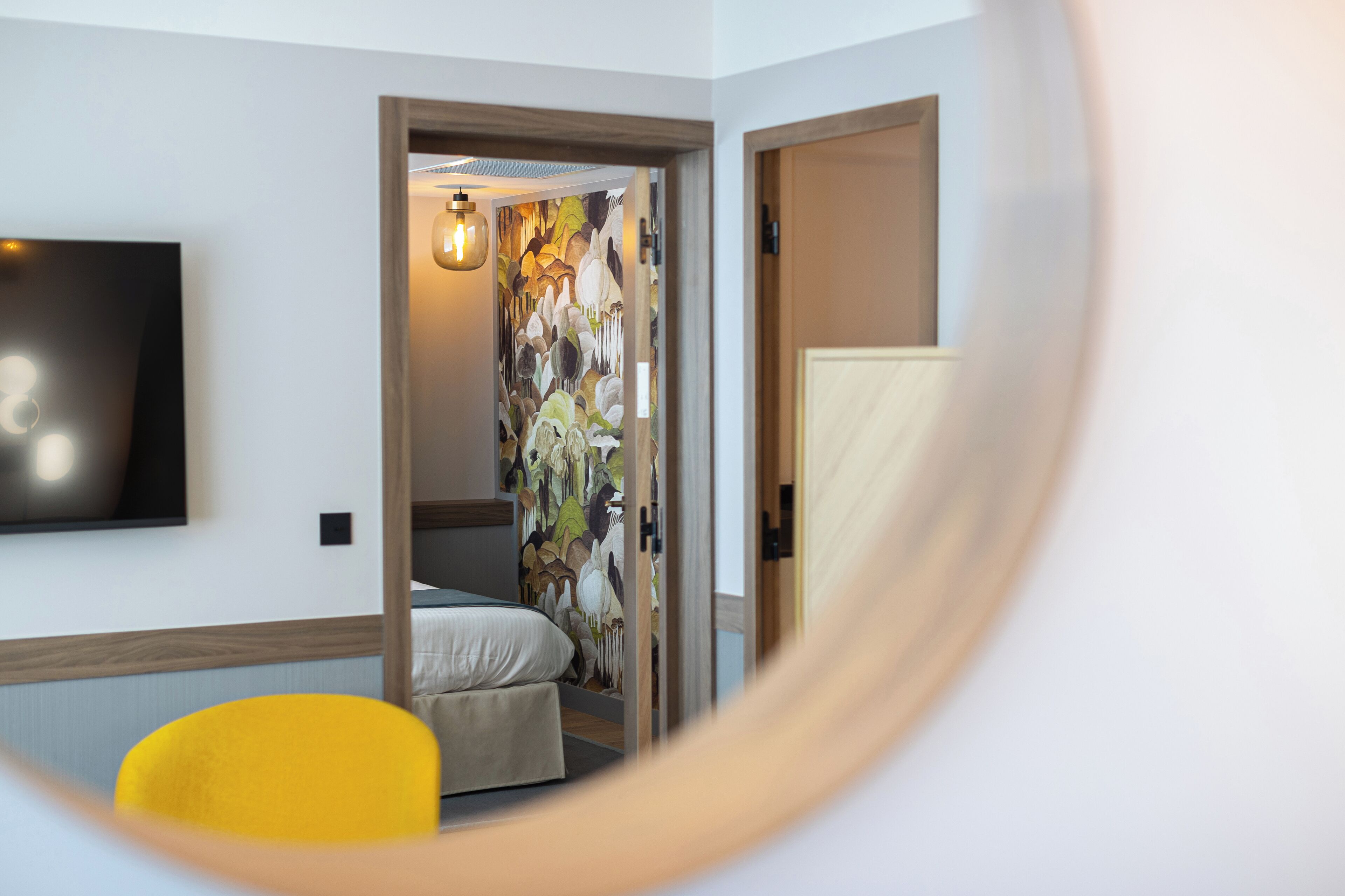 A hotel room with a bed, a chair, a TV, and a door leading to another room.
