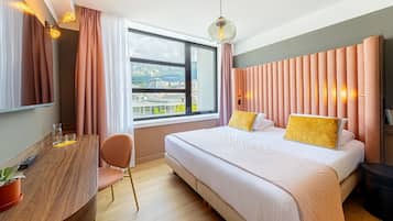 A modern hotel room with a large bed, a wooden desk, a chair, and a view of the city through the window.