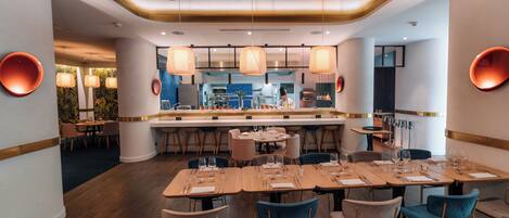 Un restaurante moderno con una barra central, varias mesas para comer y un chef trabajando.
