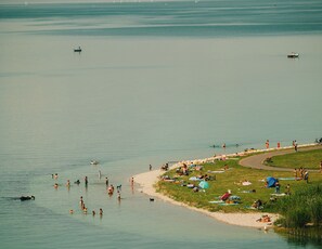 Une zone au bord du lac où l’on peut se baigner et prendre des bains de soleil, une plage de sable et une pelouse où sont installées des tentes et des parasols.