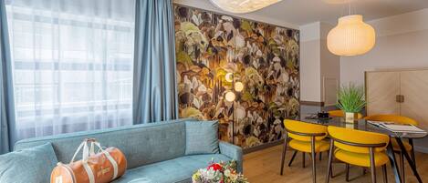 Una sala de estar moderna con un sofá, una mesa de comedor con sillas amarillas y una pared decorada con un mural de temática natural.