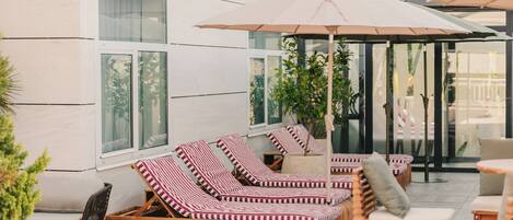 Un espacio al aire libre con mesas y sillas de lounge, sombrillas, una mesa de madera y una planta en maceta.