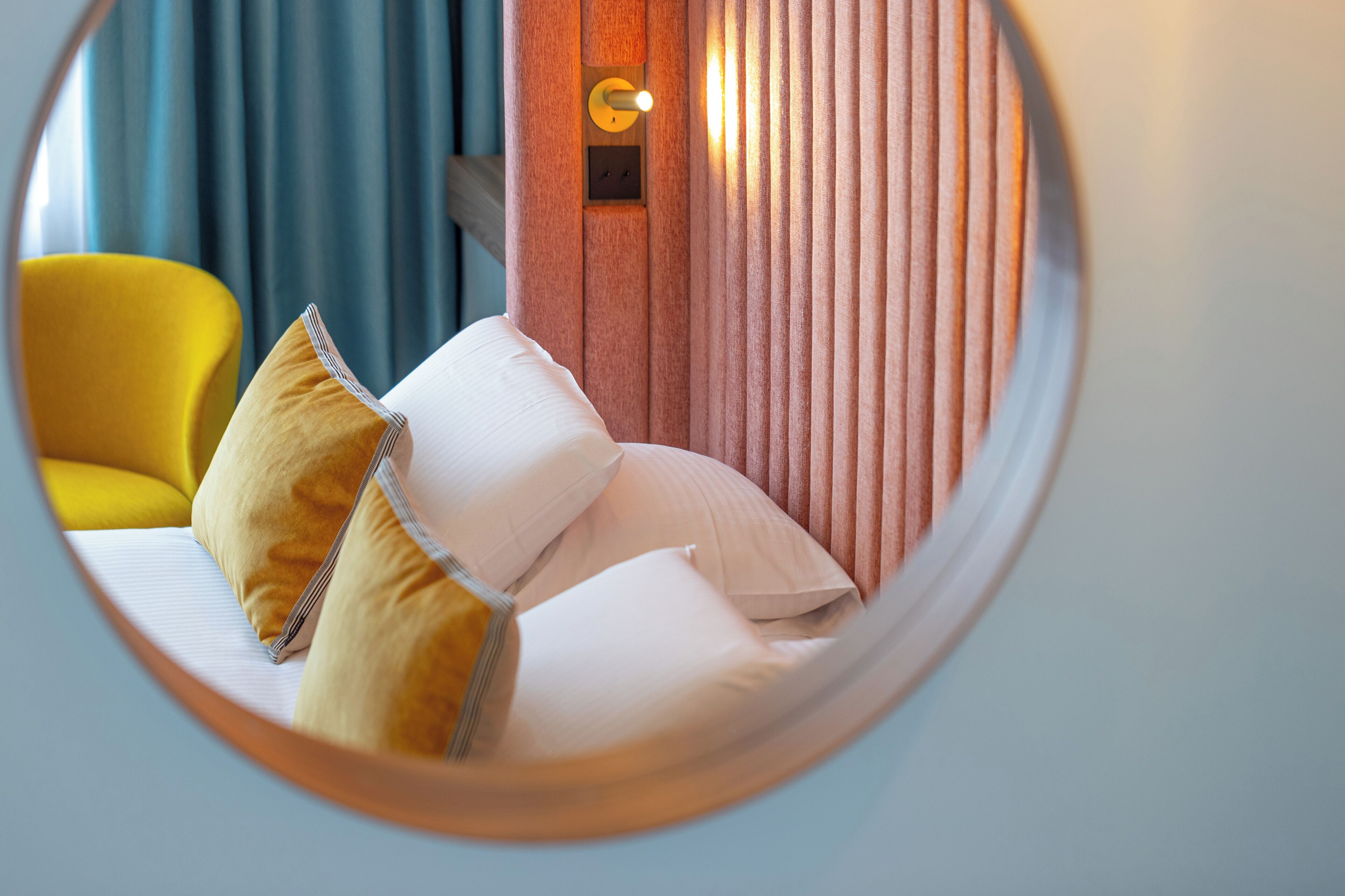 A circular view of a hotel room with a bed, pillows, and a wall-mounted light fixture.