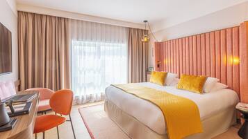 Ein Hotelzimmer mit einem großen Bett, einem Schreibtisch mit einem Laptop, einem Sessel und einem Fernseher.